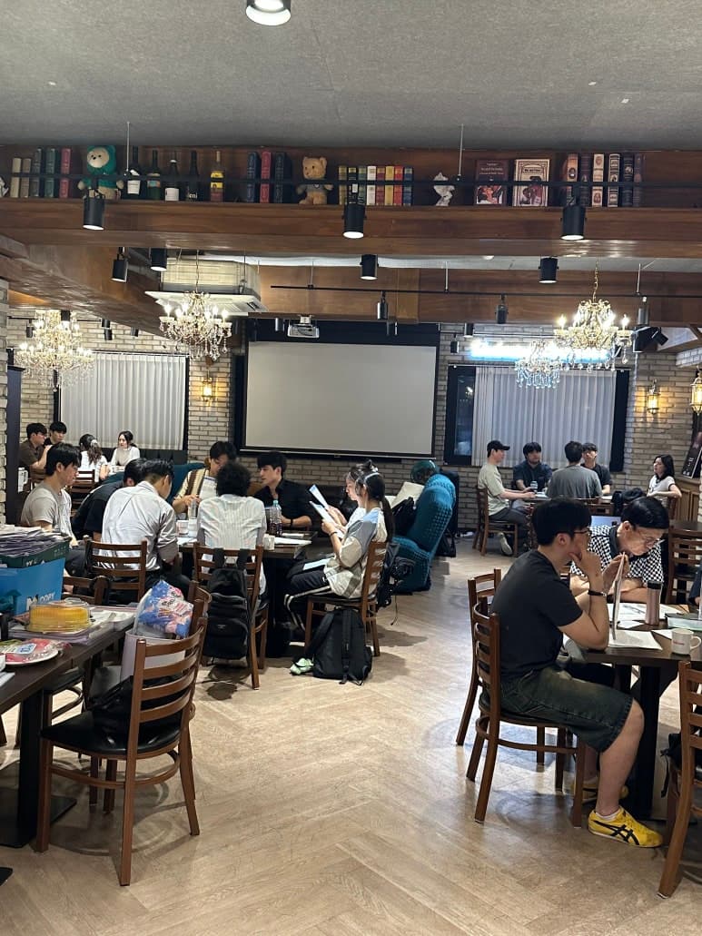 여러 테이블에 참여자들이 앉아 있는 실내 전경
